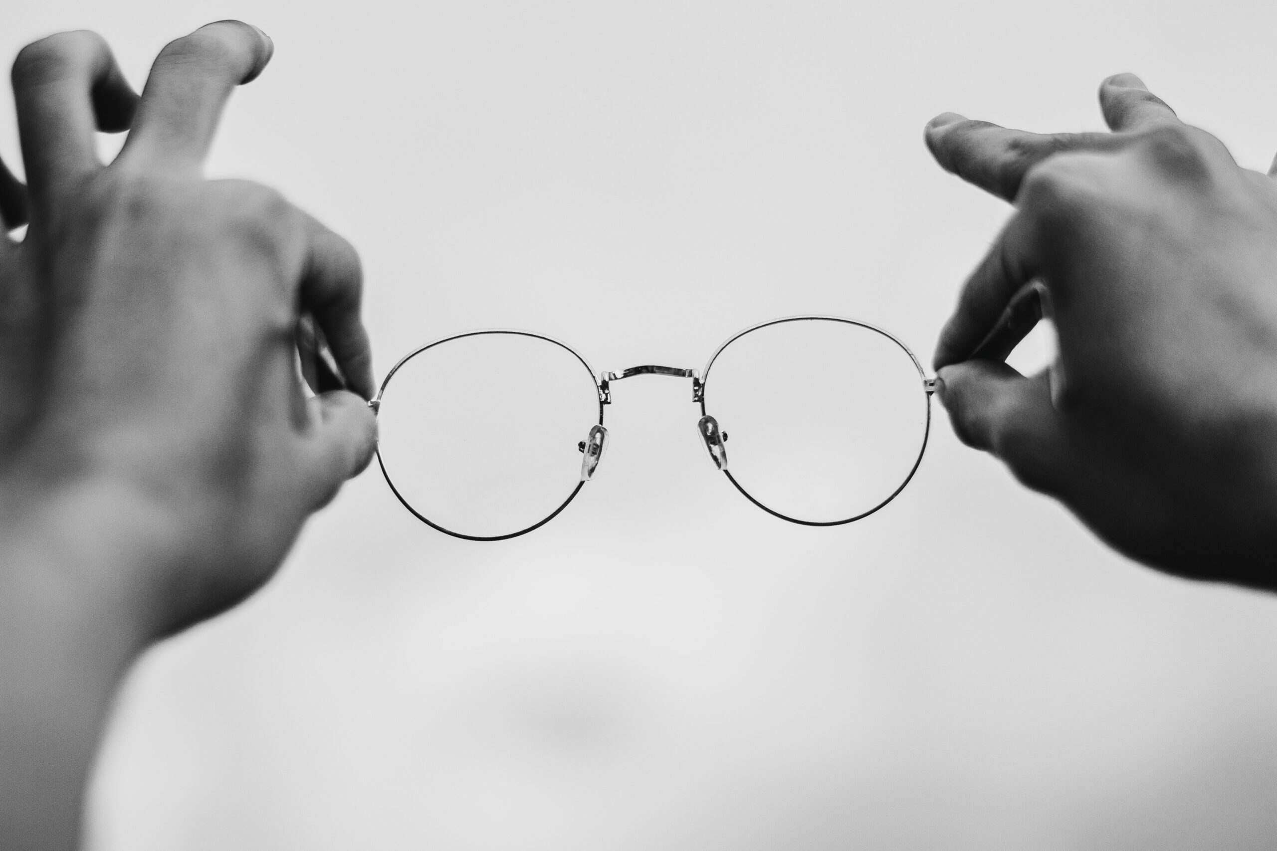 Artistic black and white photo showing hands holding eyeglasses in a minimalist setting.